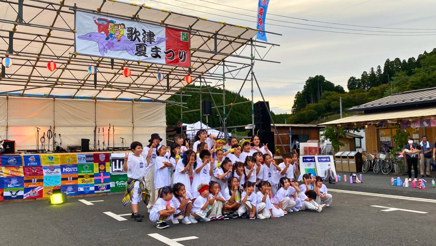子どもたちと大人がステージ前で白い衣装を着て集合写真を撮っている様子の写真