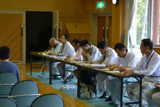 長机に並んで座る参加者たちが資料を見たり記入したりしている様子の写真