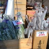 箱に入ったごぼうと長ネギが束ねて並べられ、それぞれに値札が貼られて販売されている様子の写真
