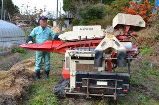 農業機械の脱穀機の前に作業服の男性が立っている写真