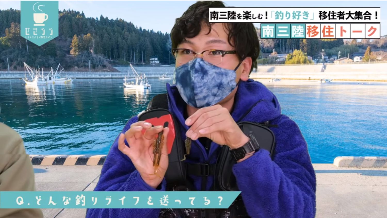 青い服と釣り用ベストを着けた男性が港のバーチャルセットを背景に、両手で釣り具の疑似餌を見せて説明しており、左下には「どんな釣りライフを送ってる？」と書かれた質問が表示されているYouTubeが表示された画面キャプチャ