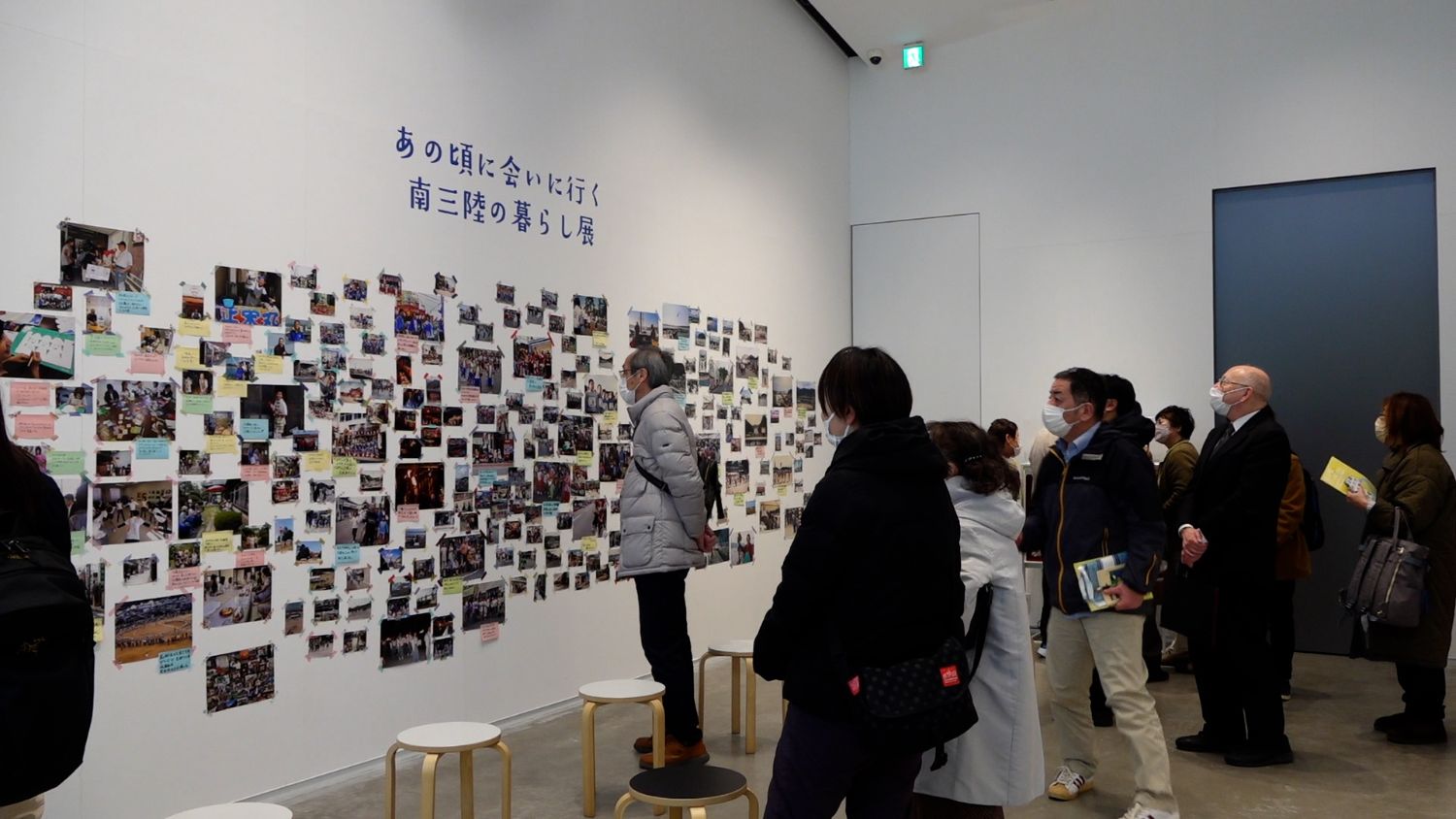 壁にたくさんの写真とメッセージカードが貼られており、人々が立ち止まってそれらをじっくり見ている方々の写真