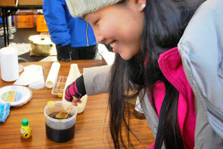 ニット帽をかぶった女性が笑顔で、紙カップに入ったタレに串をつけて味わおうとしている写真