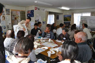 参加者が真剣な表情で話を聞きながら、テーブルを囲んでまちづくりの話し合いに参加している様子の写真