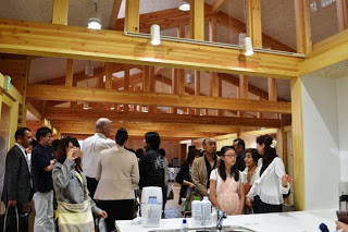 木のぬくもりが感じられる室内で、多くの人が見学や歓談をしている様子の写真