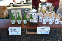 テーブルの上に日本酒の瓶が並べられ、それぞれの銘柄と価格が手書きの札で表示されている様子の写真