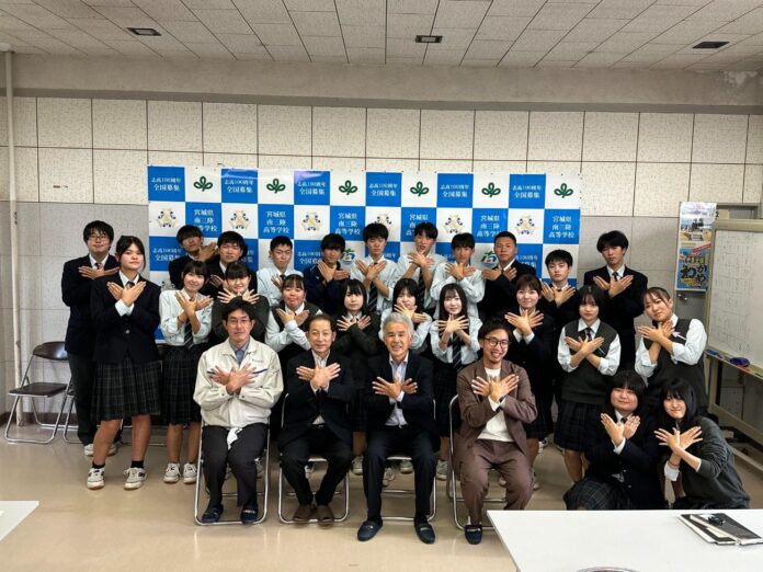 高校生と関係者全員が笑顔で、両手で蝶のようなポーズをとった集合写真