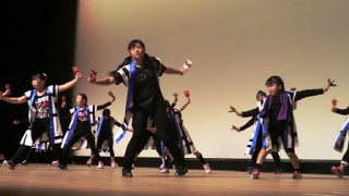 黒を基調に白と青のアクセントが入った衣装を着た子どもたちが舞台上で息の合った踊りを披露している戸倉小心輪海（とぐらしょう しんわかい）の郷土芸能発表の写真