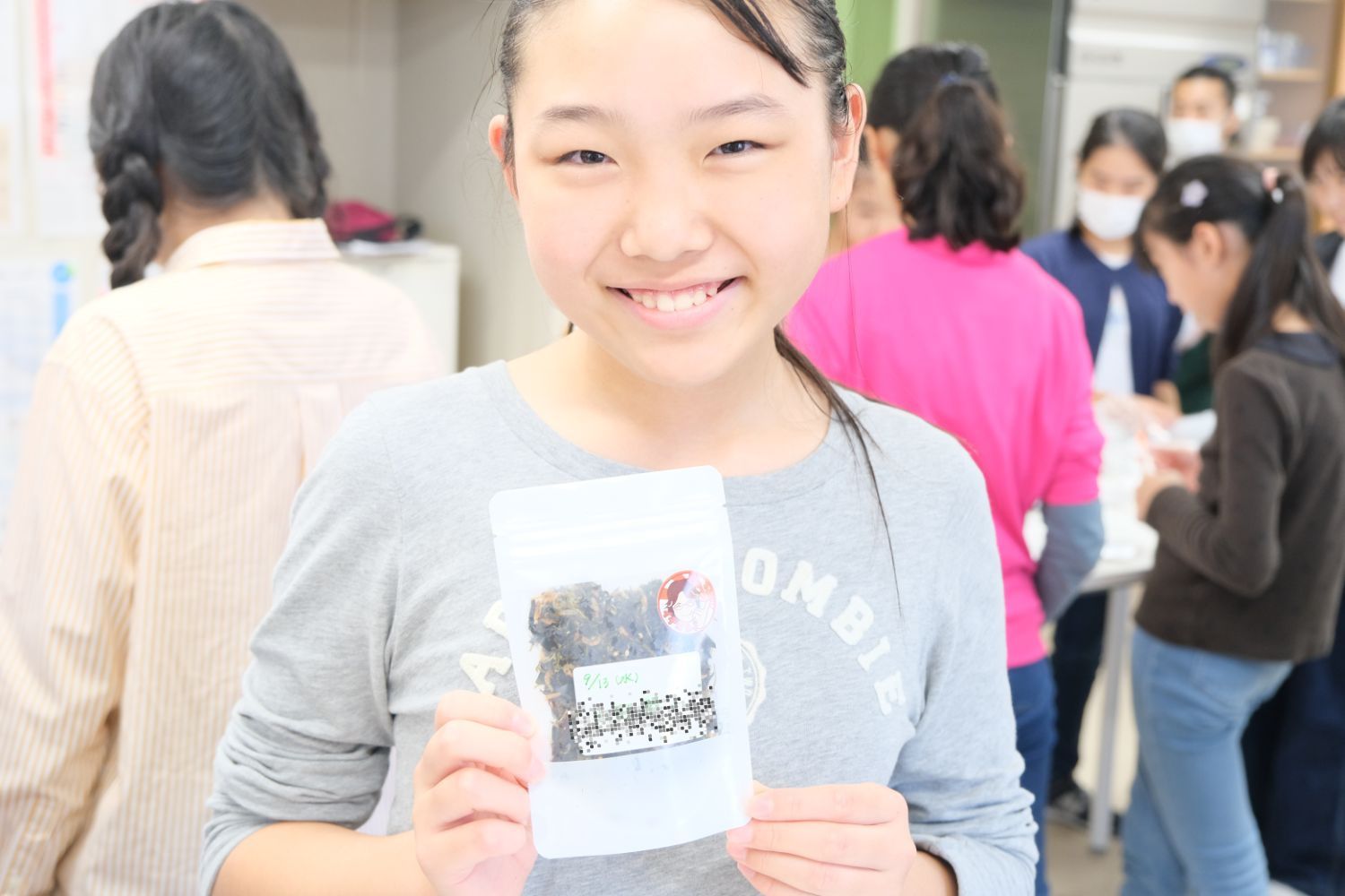 女の子が笑顔で、自分で作った海藻のパッケージを持ってカメラに見せている写真