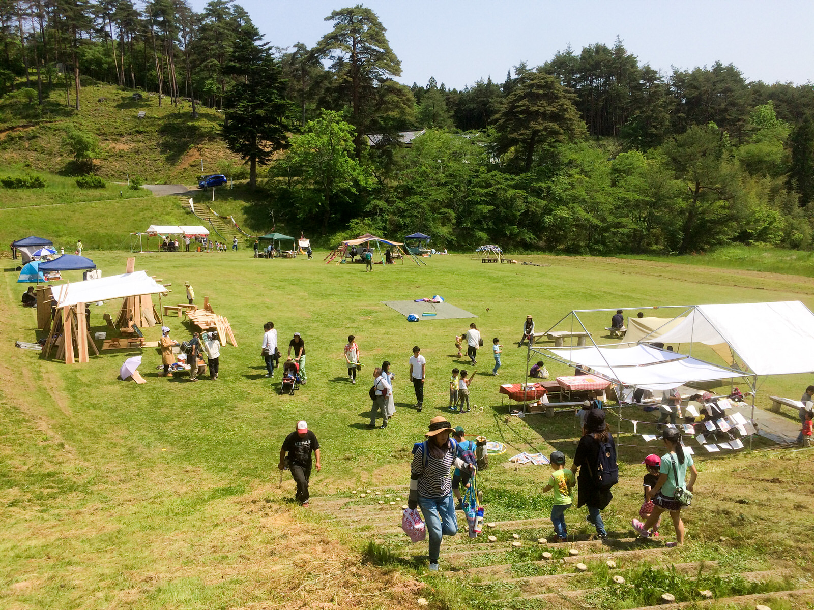 広々とした芝生の上に複数のテントが設営され、子どもや大人が遊びを楽しんでいる様子の写真