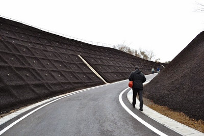 黒い法面で囲まれた曲がりくねった舗装道路の坂道を人が歩いている写真