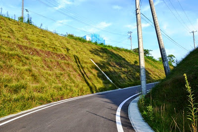 草の生えた斜面の間を舗装された新しい道路が右に曲がりながら伸びている写真
