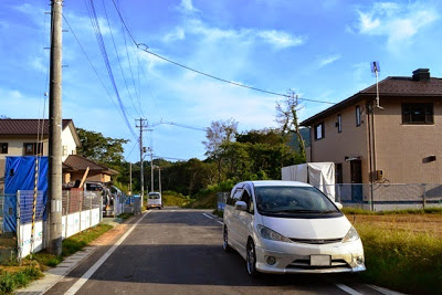 晴れた日に新しい家が建ち並ぶ静かな住宅地の舗装道路の端に白い車が停まっている住宅街の写真
