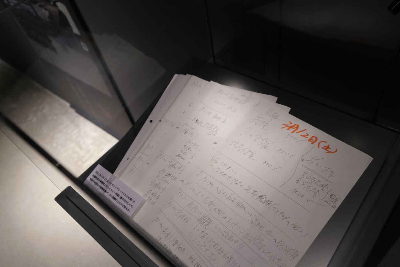 震災直後（3月12日・土曜日）のメモで、避難状況や支援物資などに関する記録が展示された写真