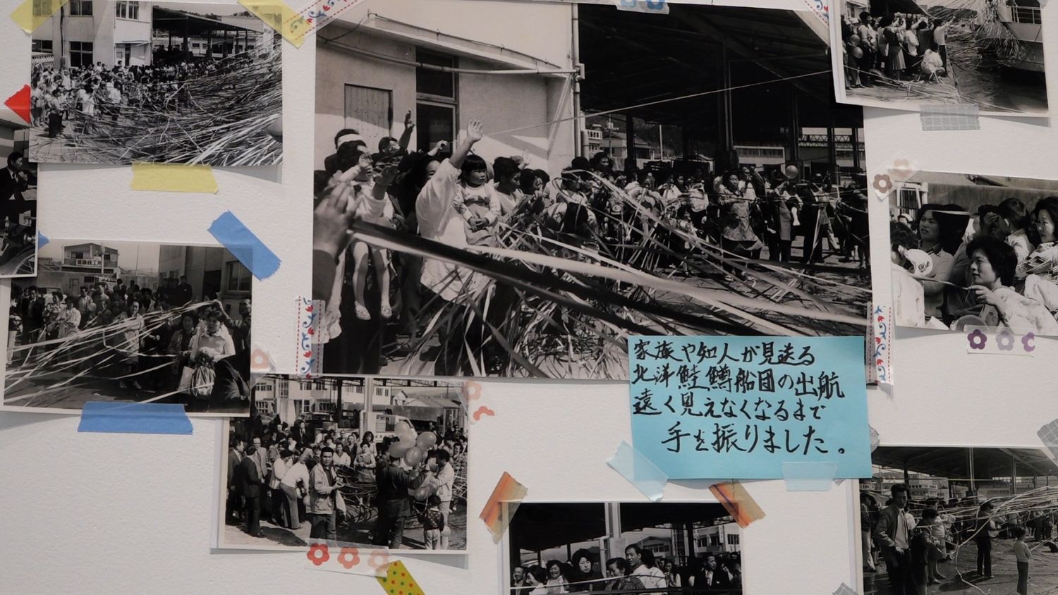 家族や知人が港から紙テープで見送る中、漁船が出航していく様子を記録した白黒写真が、青い手書きメッセージとともに展示されている写真