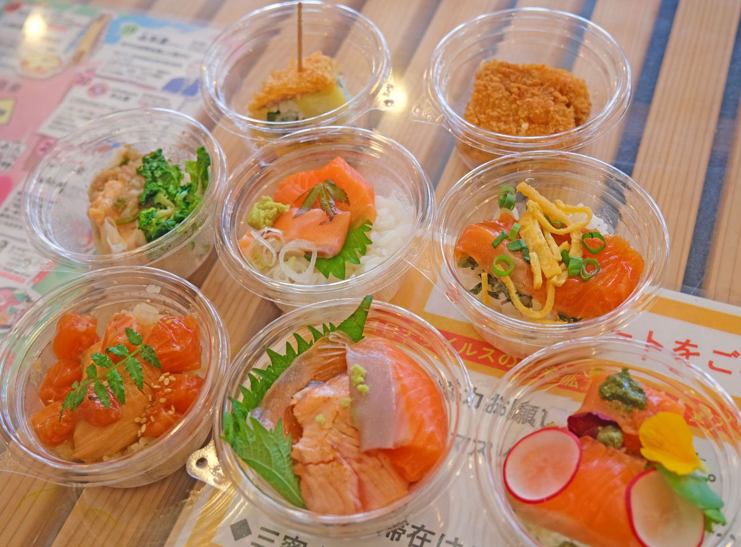 小さな透明なプラスチック容器に盛られた色とりどりのサーモンを使った料理が8種類並んでいる写真