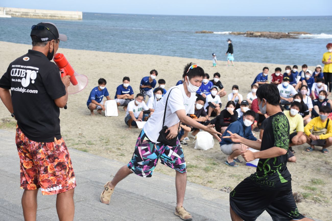 砂浜で観客が見守る中、2人の選手がジャンケンをしている様子を右側から撮影した写真