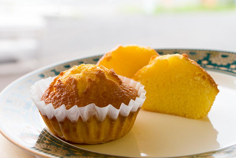 花柄の縁の丸皿にシートに入ったままの商品と、半分にカットされ黄色の断面を向けた、お山のマドレーヌの写真