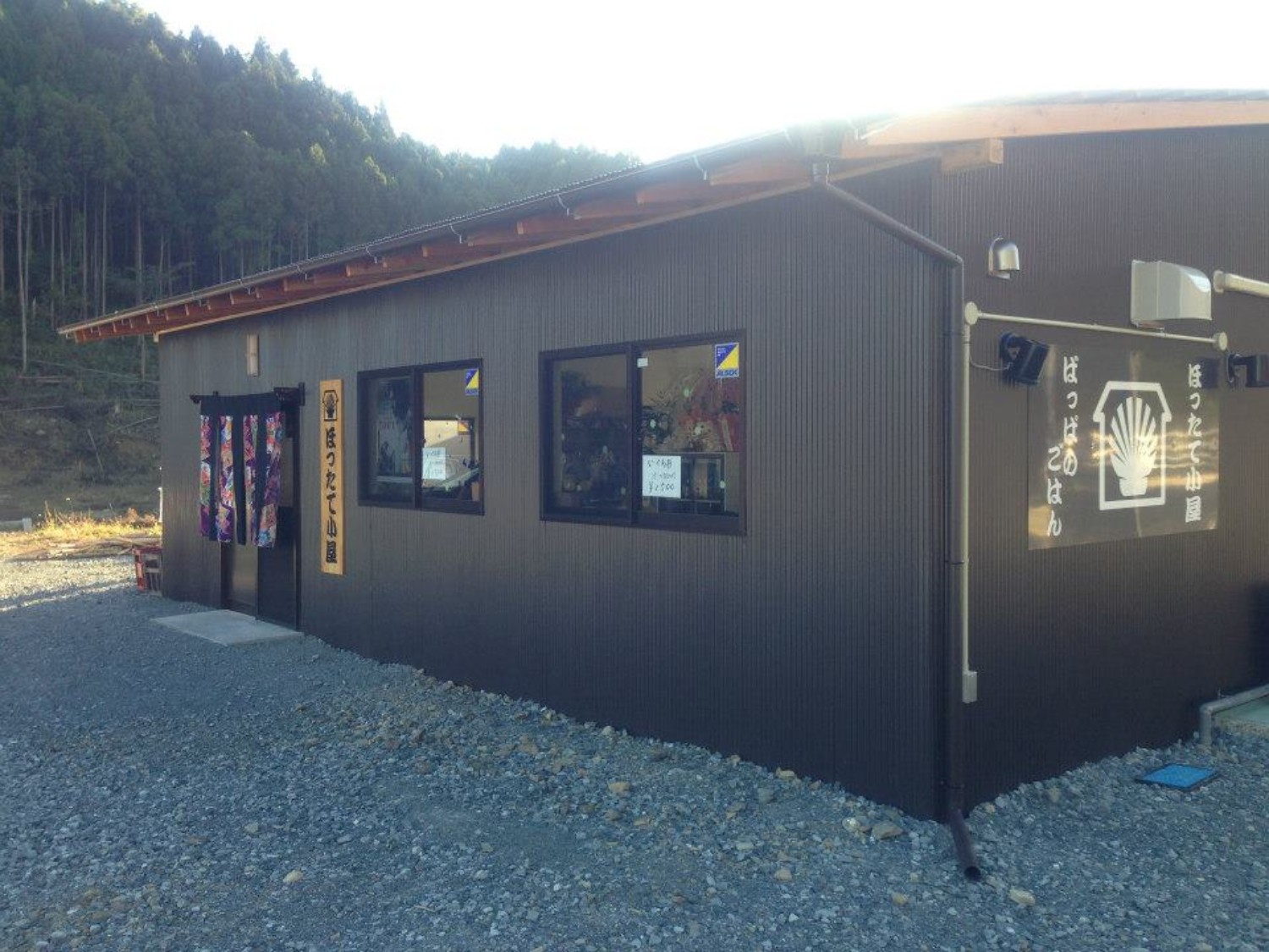 黒い外壁の平屋の建物の暖簾がかかった入口横に「ほったて小屋」と書かれた看板が取り付けられている、ほったて小屋の外観写真
