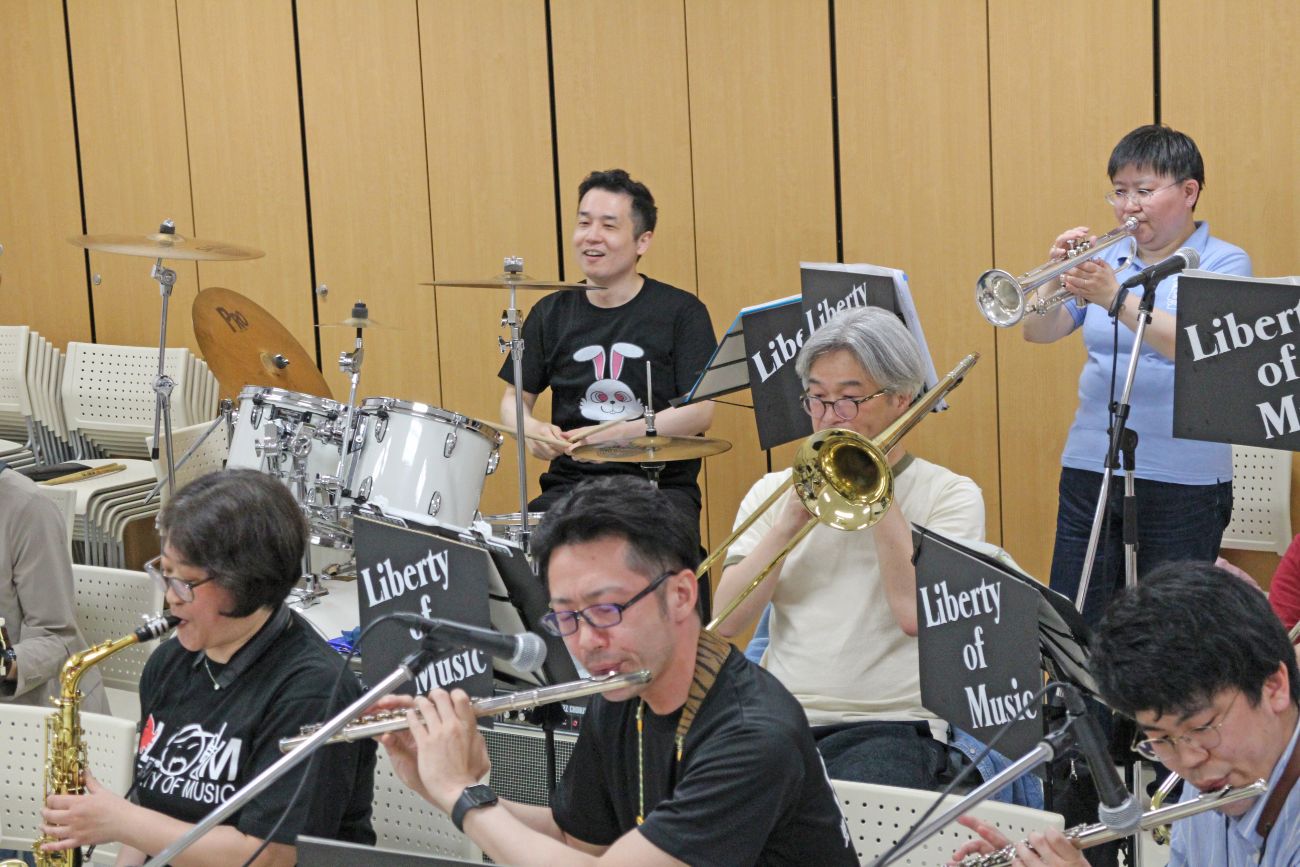 フルートやサックス、トランペットにドラムを演奏するLiberty of Musicのメンバーが楽しそうに練習している演奏中の写真