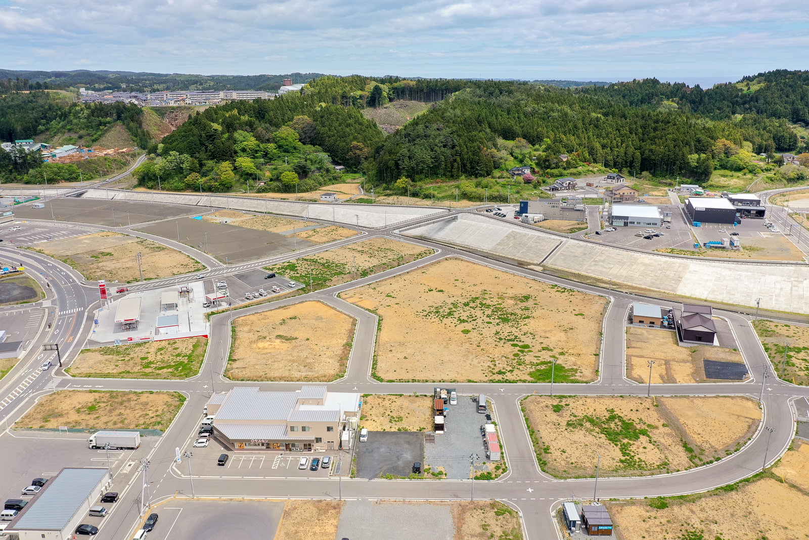 緑豊かな丘陵地帯を背景に、整然と区画整理された土地と舗装された道路が広がっている風景の写真