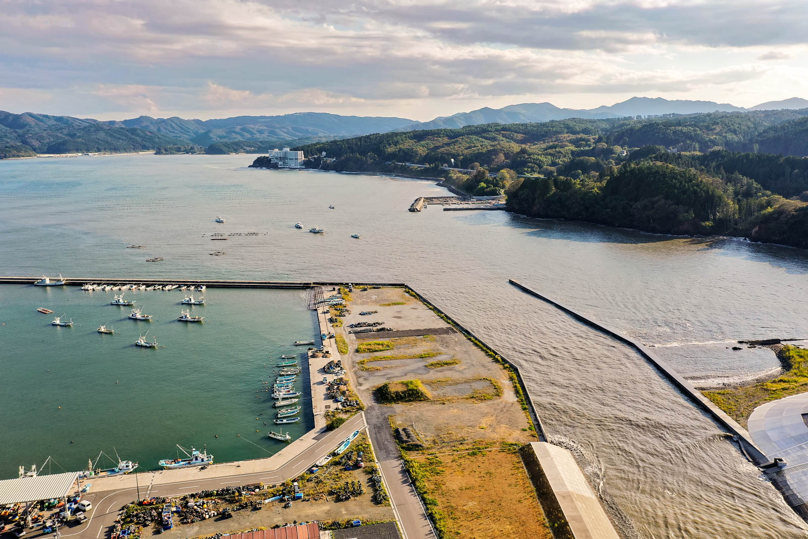 防波堤に囲まれた港の内側に整然と並ぶ漁船、その先に湾口と対岸の山々が広がる湾中央の写真