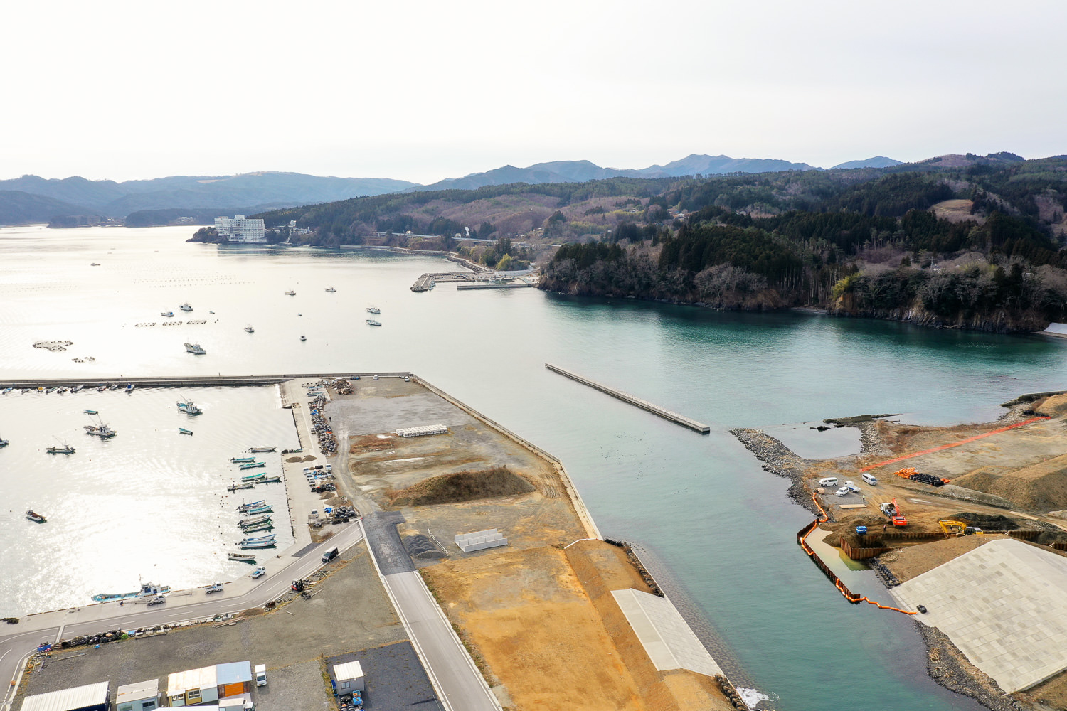海に面した港を上空から撮影した写真で、複数の船が静かに停泊しており、その周囲には緑豊かな山々が広がっている港の写真