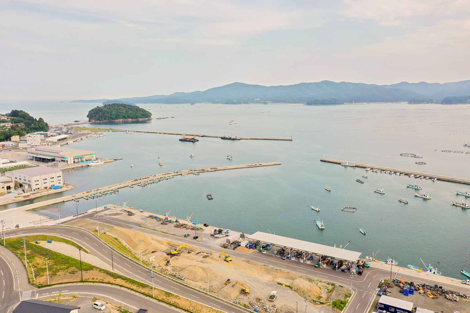 海に面した港町の風景で、複数の船が停泊しており、背景には山々が広がっている写真