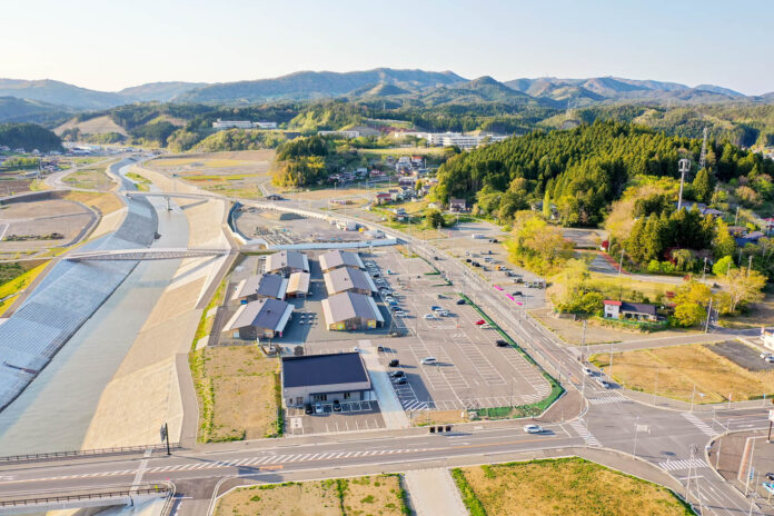 手前には広々とした駐車場と複数棟の平屋建て施設が並んでおり、中央を流れる川は高い護岸でしっかりと囲まれており、両岸の防災インフラが新しく整備されている様子が見て取れる写真