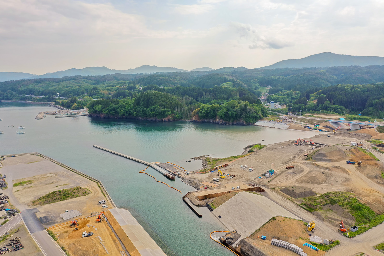 海に面した港湾工事現場で、岸辺に重機や資材が配置され、周囲には海と空が広がっている写真