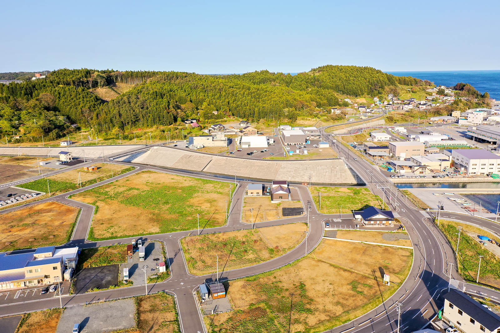 手前には新しく整備された道路網と区画が広がっており、まだ更地の部分が多く見られところどころに新築の建物が点在しており、住宅や小規模施設として利用されている写真