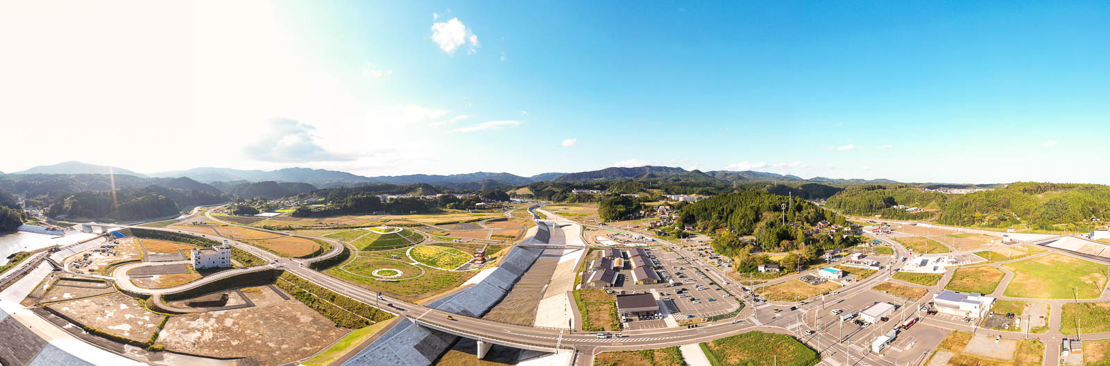 広大な谷あいに整備された人工河川とその周囲の復興住宅地や商業施設、山々に囲まれた自然豊かな地域が俯瞰できる、被災後の再開発全体像を広角で捉えた写真