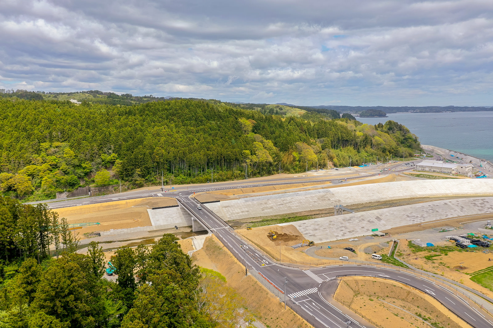 緑豊かな森林に囲まれた海岸沿いに道路と防波堤が整備されており、自然と人工構造物が調和する風景を写した海岸沿いの道路と防波堤の写真