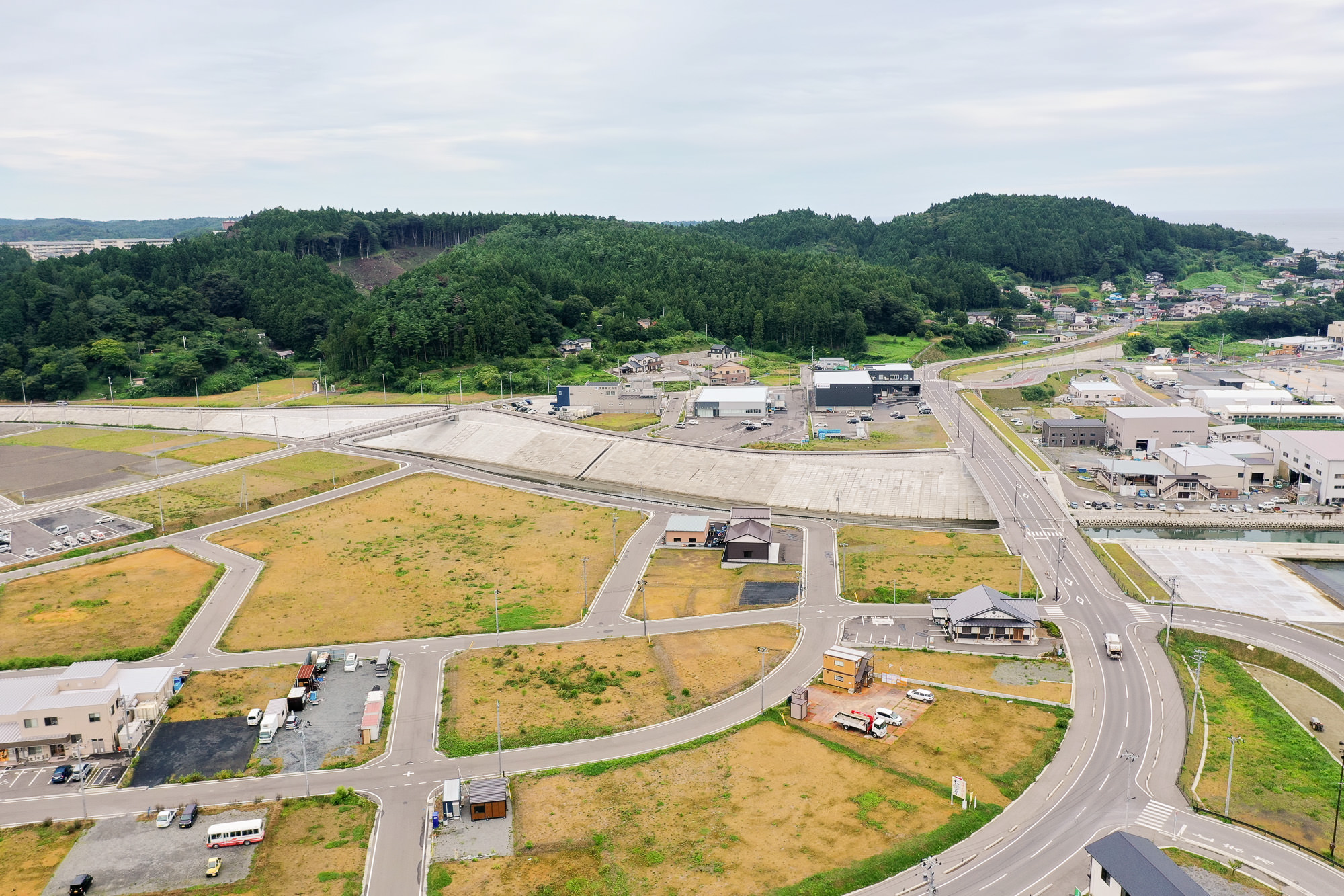 六角形状の区画が並ぶ造成地と背後に広がる山林と住宅街が見える、再開発が進むまちの写真