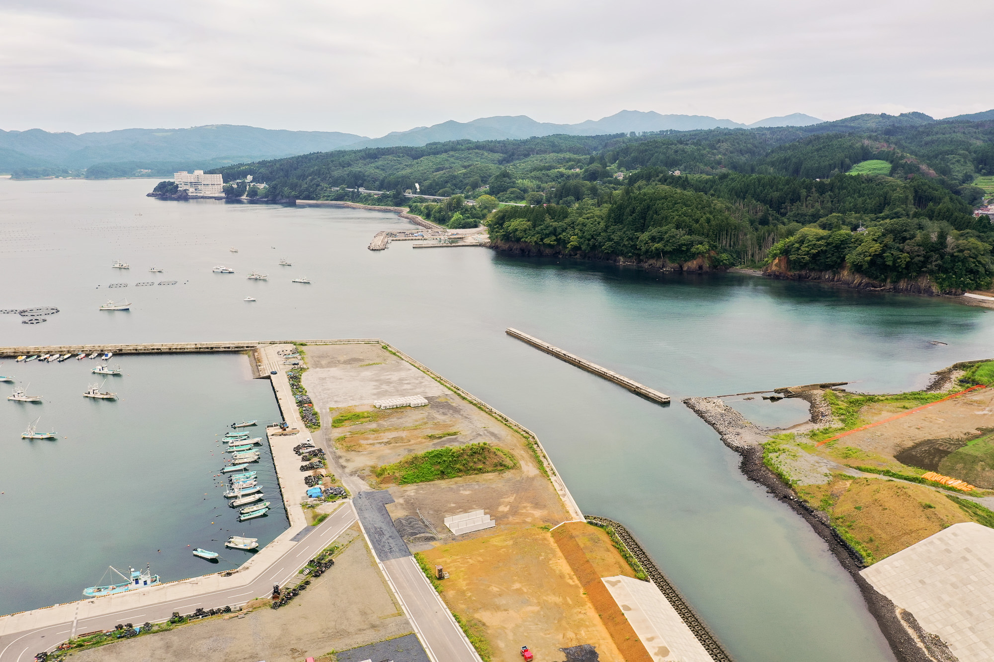 防波堤に囲まれた右奥の静かな湾と、その先に見える森林に囲まれた岬、周囲に建物がない広大な空き地が特徴的な湾奥の写真