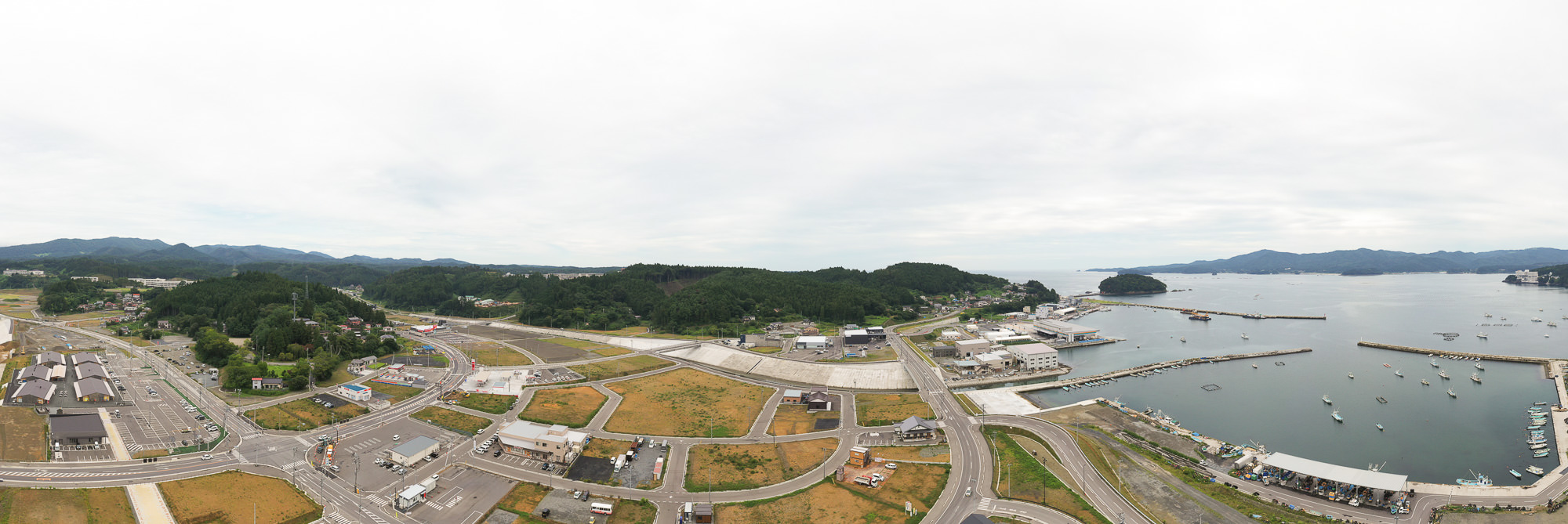 右側に海と港が広がり、左側には造成地と建物、中央に道路が湾に向かって延びる様子を俯瞰した海岸部の写真