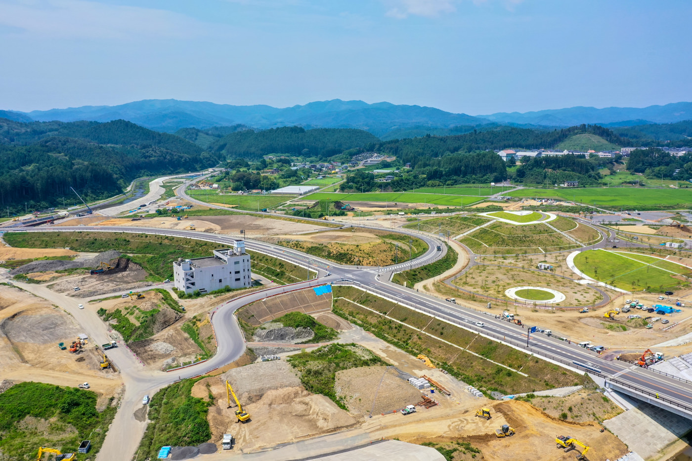 広々とした田園地帯の中に、真新しい舗装道路と関連するインフラ設備が整備されており、周囲には緑豊かな農地が広がっている風景の写真