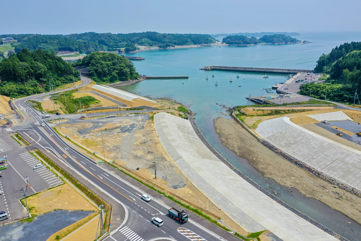 波打ち際に沿ってまっすぐ伸びる海岸沿いの道路と、それに沿って設けられたコンクリート製の防波堤が見える静かな海辺の風景の写真