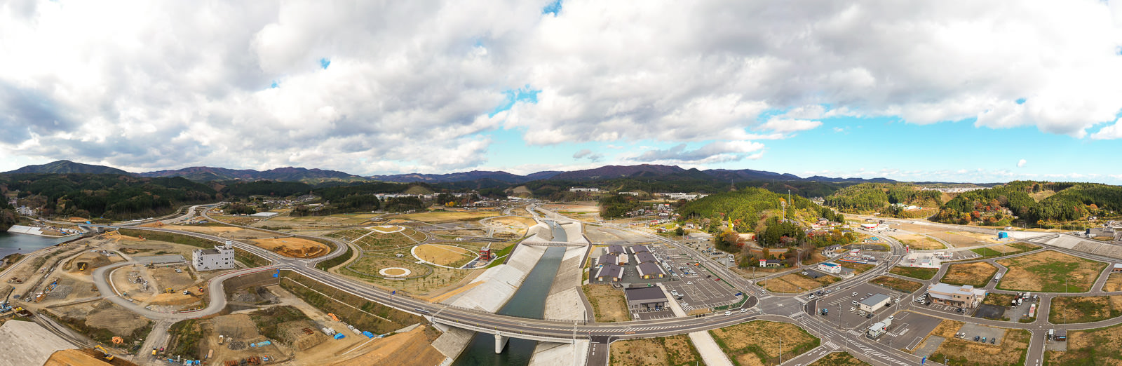 広い範囲にわたって重機や資材が配置された工事現場が広がり、その周囲には緑の木々や建物が点在している風景が写っている工事現場の写真