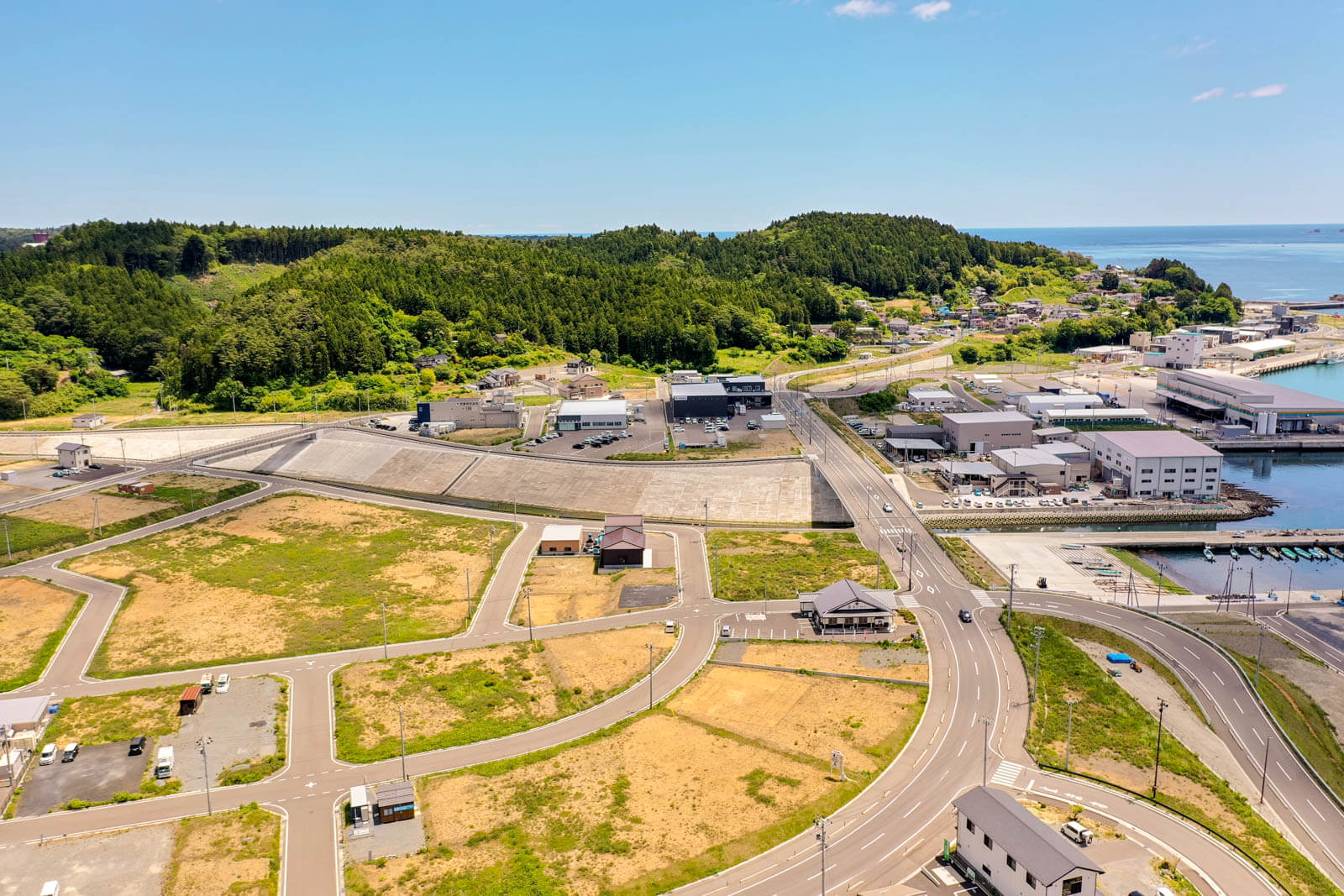 手前には新しく整備された道路と区画が広がり、まだ空き地が多く見られますが、いくつかの住宅や公共施設が建っている写真