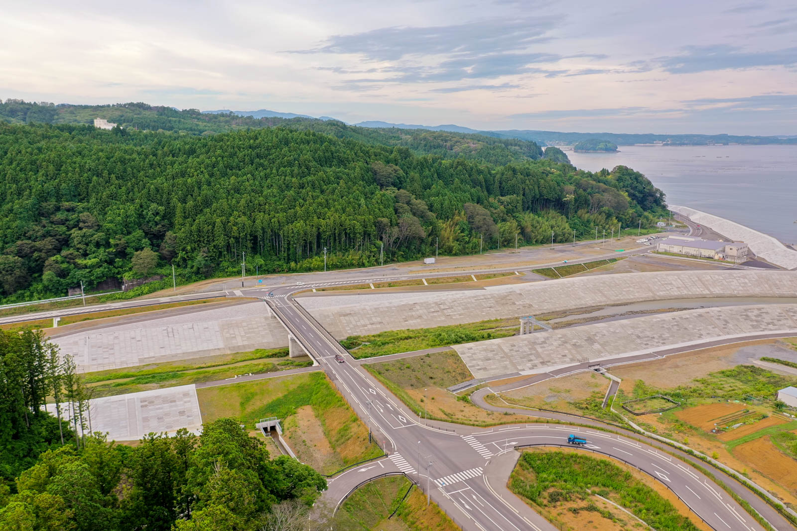 緑豊かな森林と海岸線を背景に、複数の道路が交差し、広い空き地が広がっている風景の写真