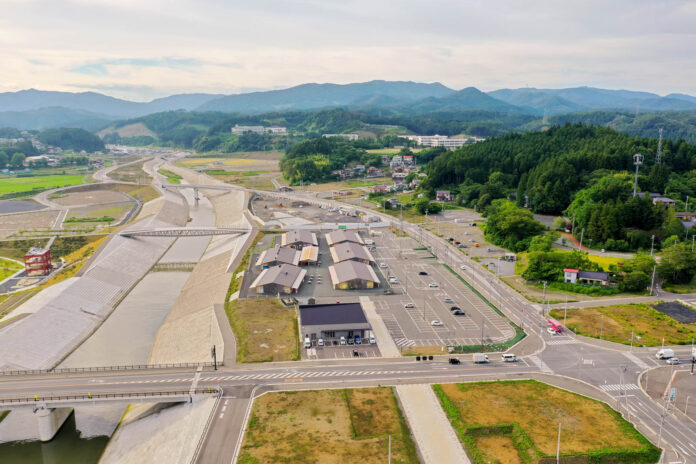 川沿いに建物と駐車場が整備されており、その奥には緑豊かな山々が広がっている田舎の風景の写真