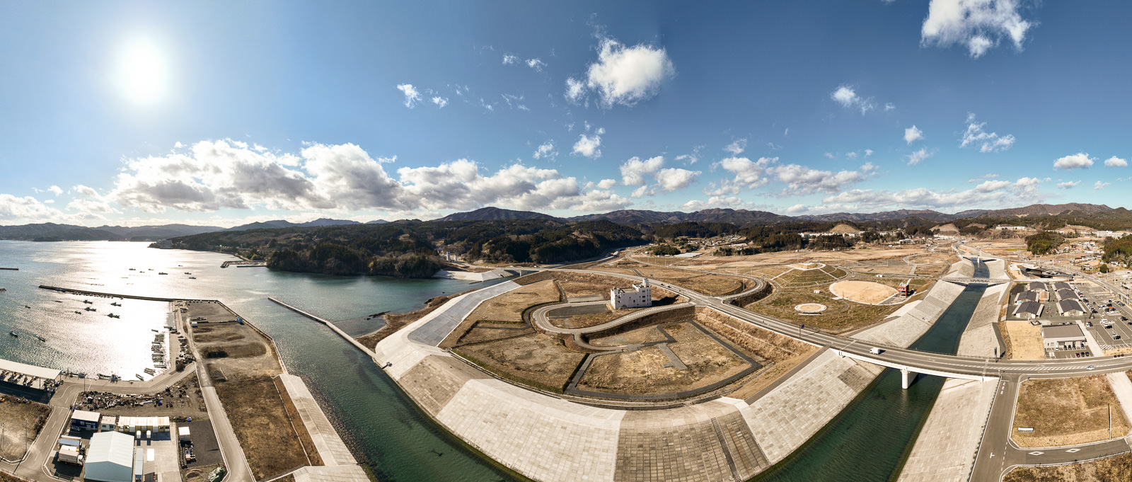 湾に注ぐ川と堤防に沿って整備された新しい街並みを広く捉え、左に海、右に山、中央に湾岸インフラが整っている風景を高台から定点カメラで撮影した写真