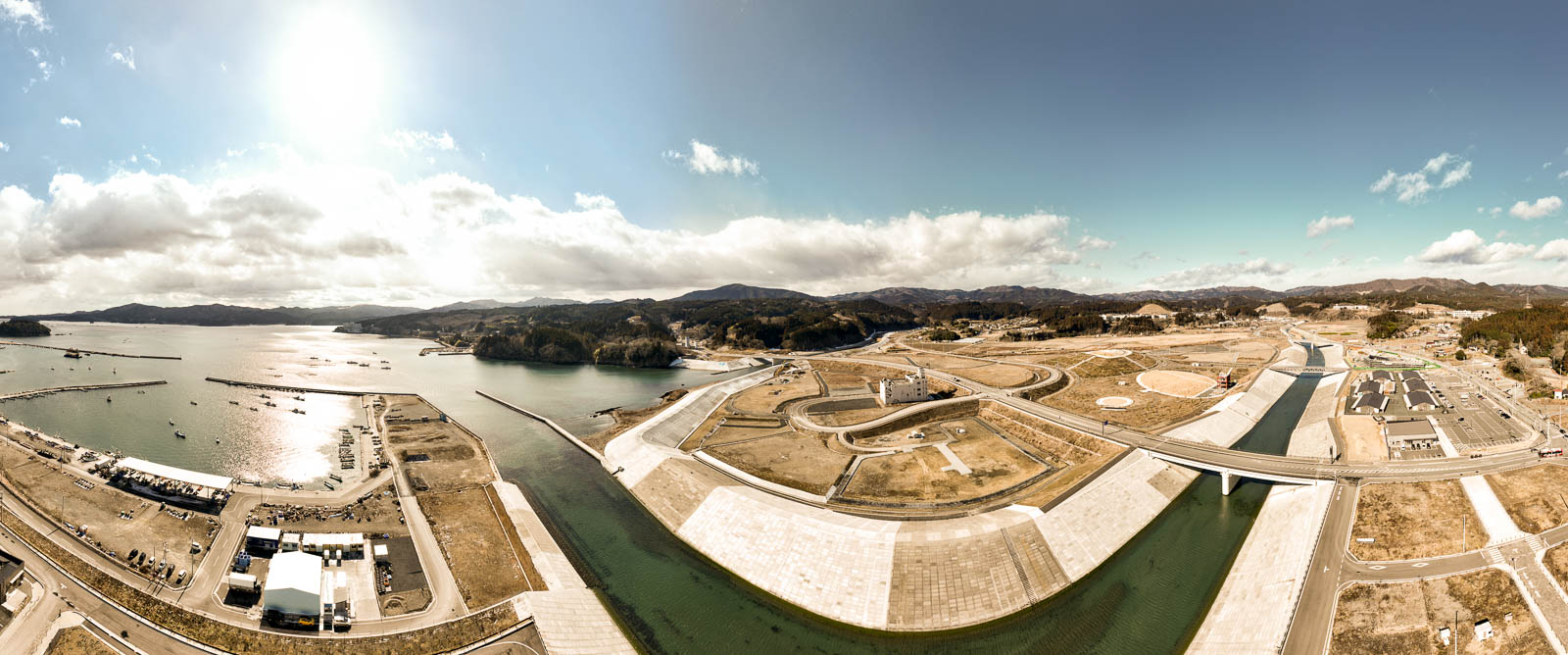湾に注ぐ川と堤防に沿って整備された新しい街並みを広く捉え、左に海、右に山、中央に湾岸インフラが整っている風景を高台から定点カメラで撮影した写真