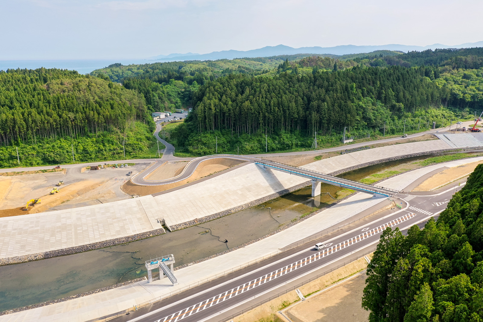 広い森林地帯の中を川が流れ、その上に橋が架かっている風景を空から見下ろした写真