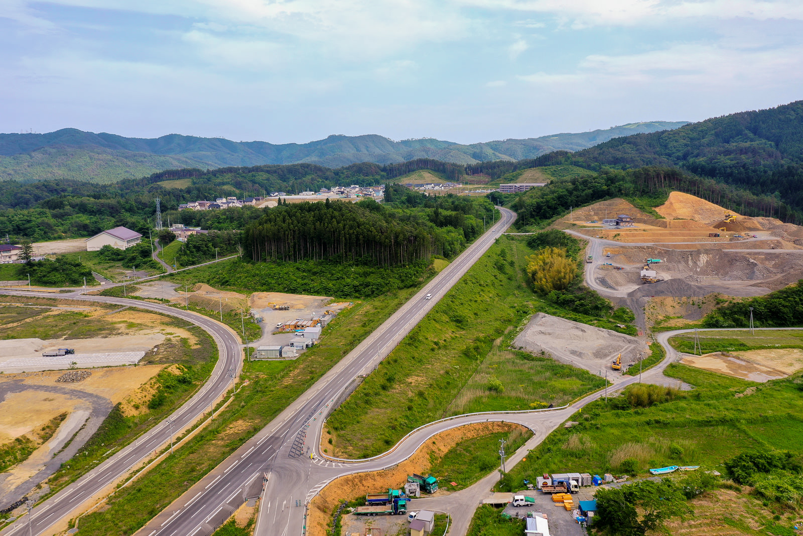 中央を道路が通り抜け、その周囲には緑豊かな丘陵といくつかの工事区域が広がる自然と開発が共存する地域の写真
