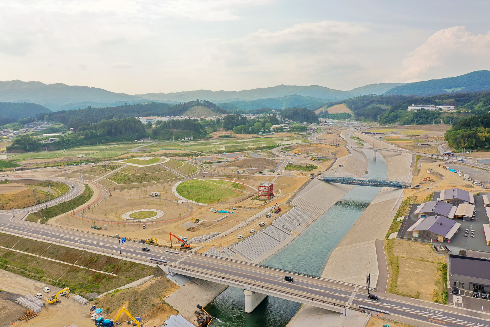 広い範囲にわたる工事現場で、川を渡る橋とその周辺の道路や建物が見える写真