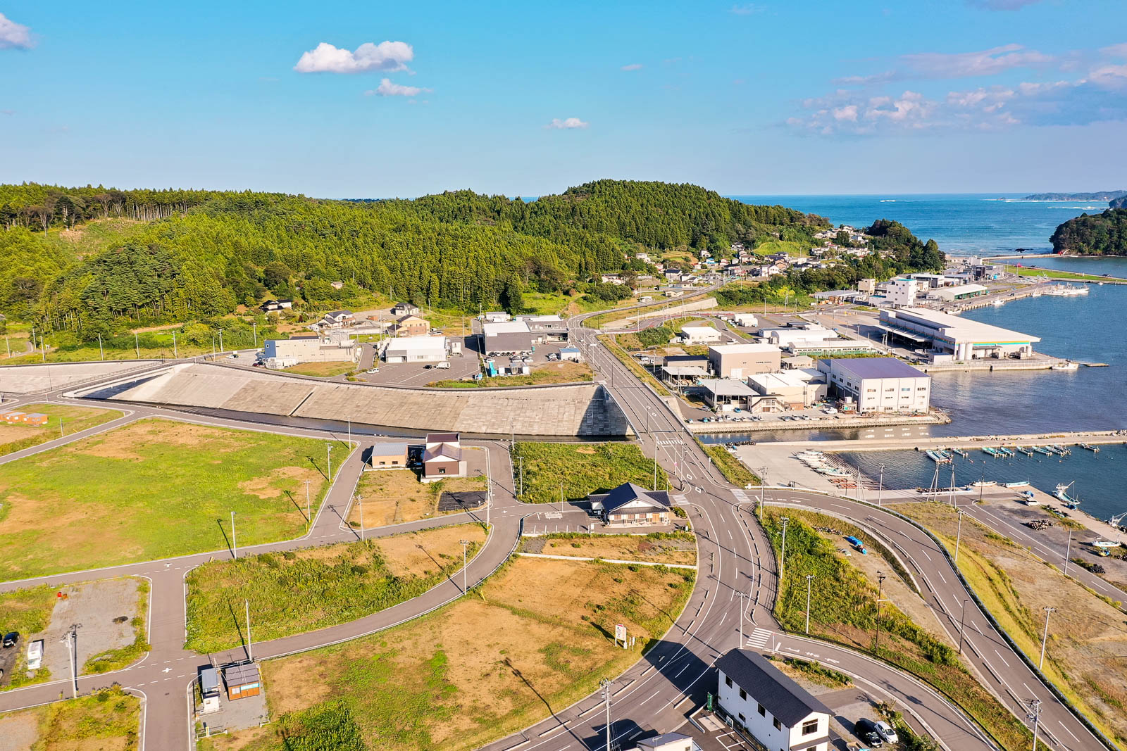 人工河川が流れ、右側に広がる市街地と住宅、そして港に続く道路と防潮堤が写され、手前に大きな交差点がある港町中心部の再開発地の写真