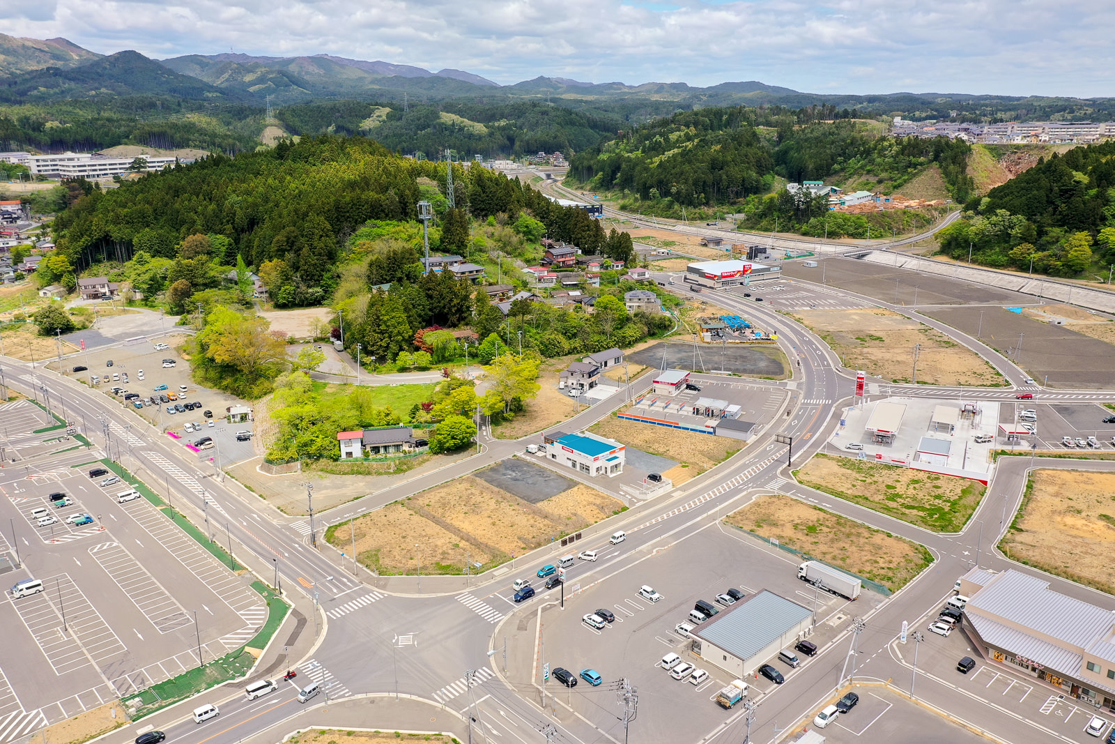 広々とした駐車場と道路に囲まれた緑豊かな丘陵地帯が広がり、自然と人の手が加わった風景が調和している様子を写した丘陵地の写真
