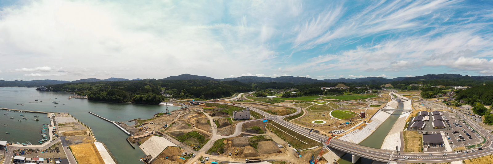 海岸沿いに広がる広大な建設現場で、道路や橋が建設中であり、周囲には緑地と山々が広がっている様子を上空から捉えた建設中の海岸地域の写真